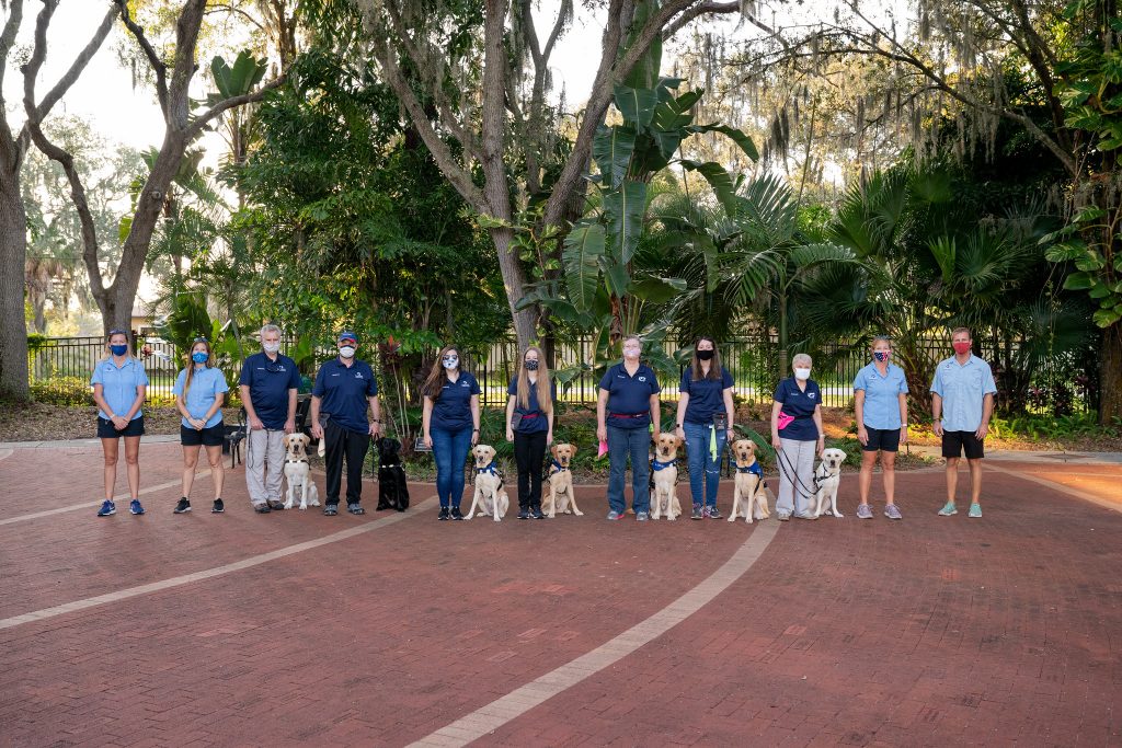 the students of guide dog class 294 stand in a brick courtyard with their new guide dogs and their instructors