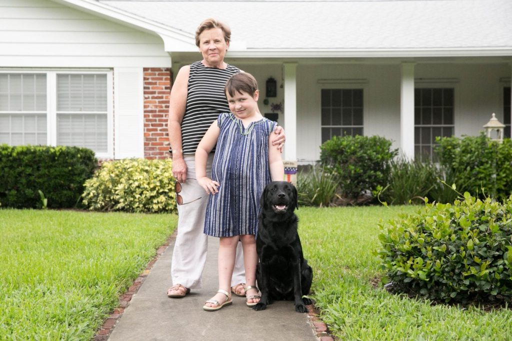A family stands in front of a house with a black lab