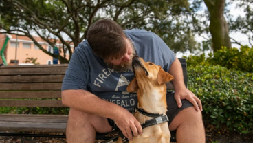 Man sits on bench leaned over and kissed guide dog