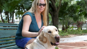 Woman sits on a bench and pets yellow labs head