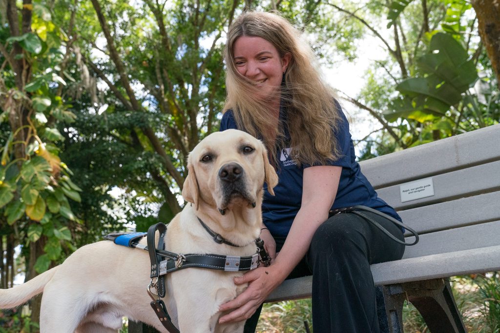 Young girl sits and pets her yellow lab guide dog