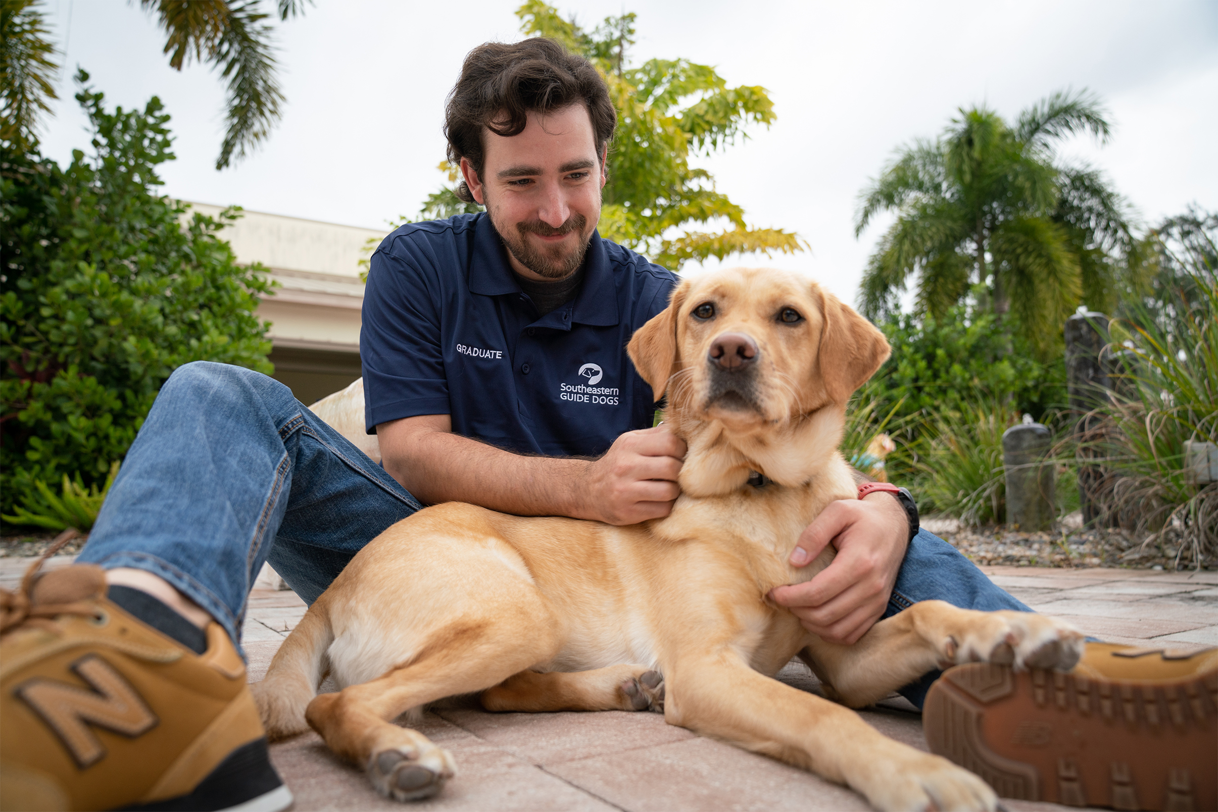 Man sits on the ground with yellow lab laying between his legs