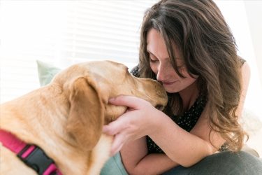 Lady smiles while she hold yellow labs head