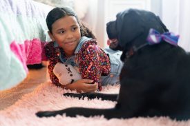 Young girl lays on belly next to black lab