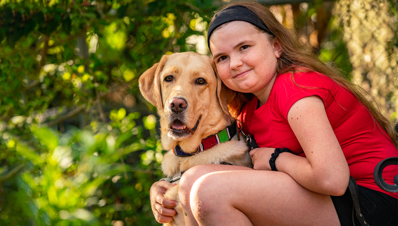 young girl in red shirt faces camera with yellow Lab guide dog