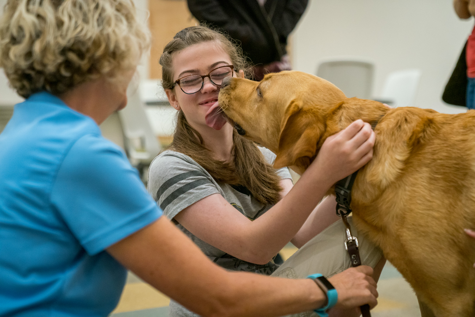 Teen girl smiles with eyes closed while yellow dog kisses her chin