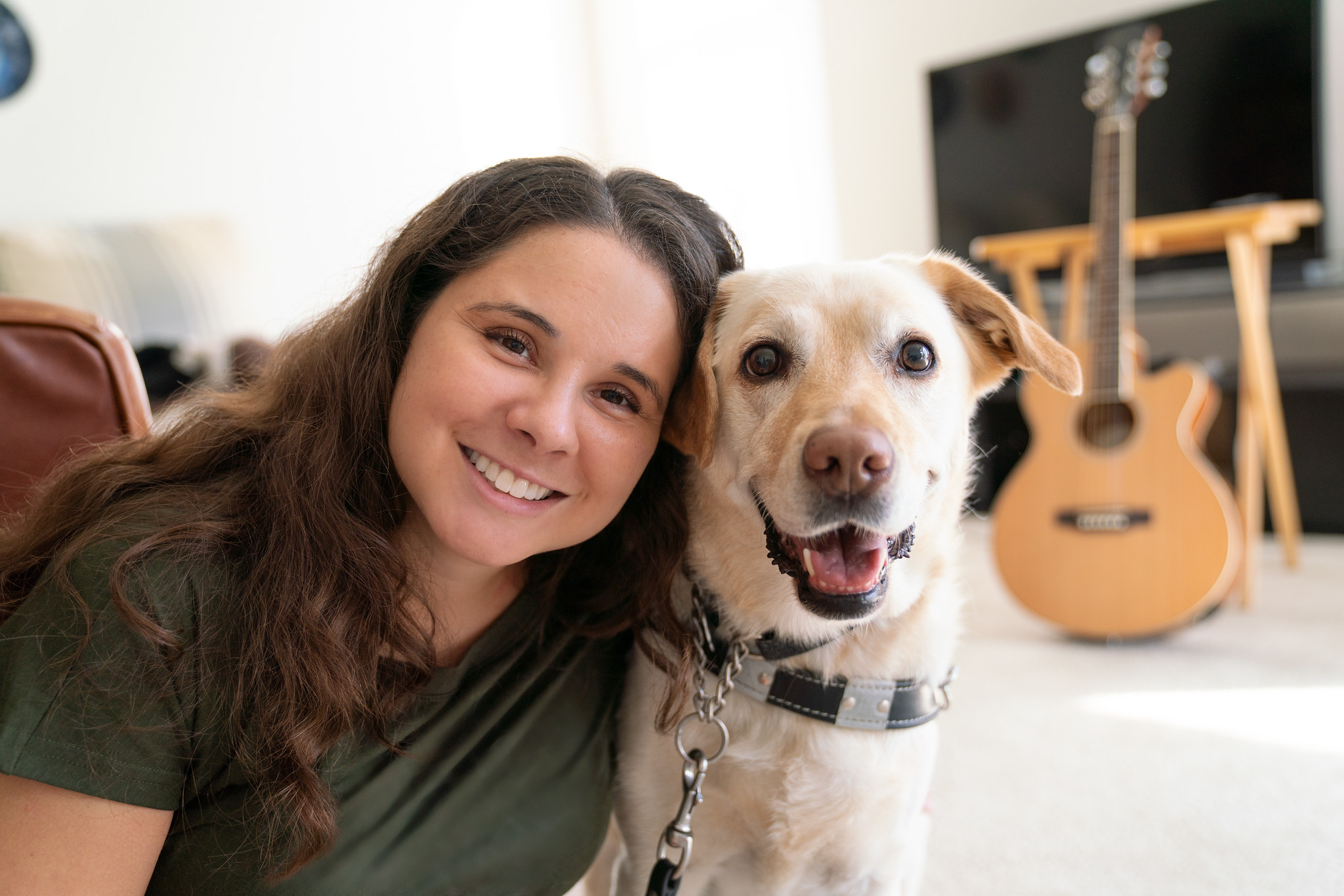 Girl smiles while she sits next to yellow guide dog who is also looking at the camera