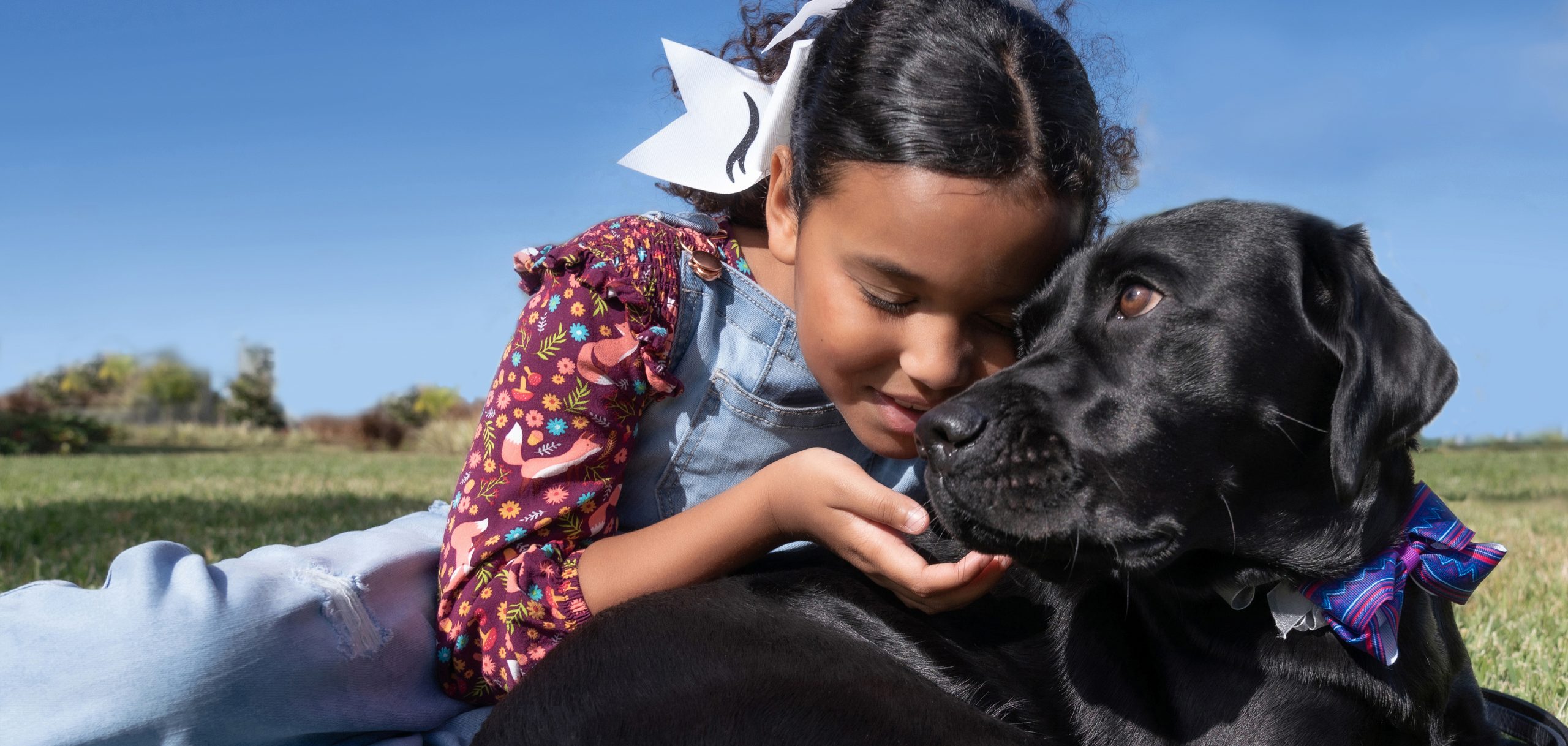Young girl smiles while she lays next to black dog with her hand touching dogs chin