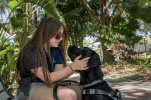 A young girl hold her black labs head and smiles down at him