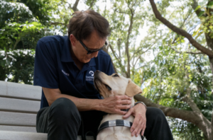 A man looks down lovingly at his yellow lab guide dog