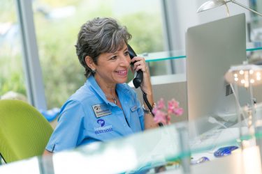 Older woman sits at desk on the phone and smiles