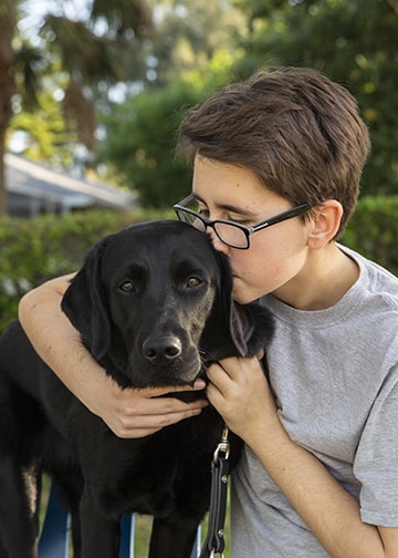 Teen girl hugs and kisses black lab