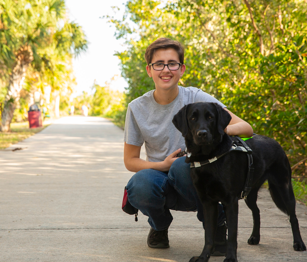 Teen girl kneels next to black lab guide dog