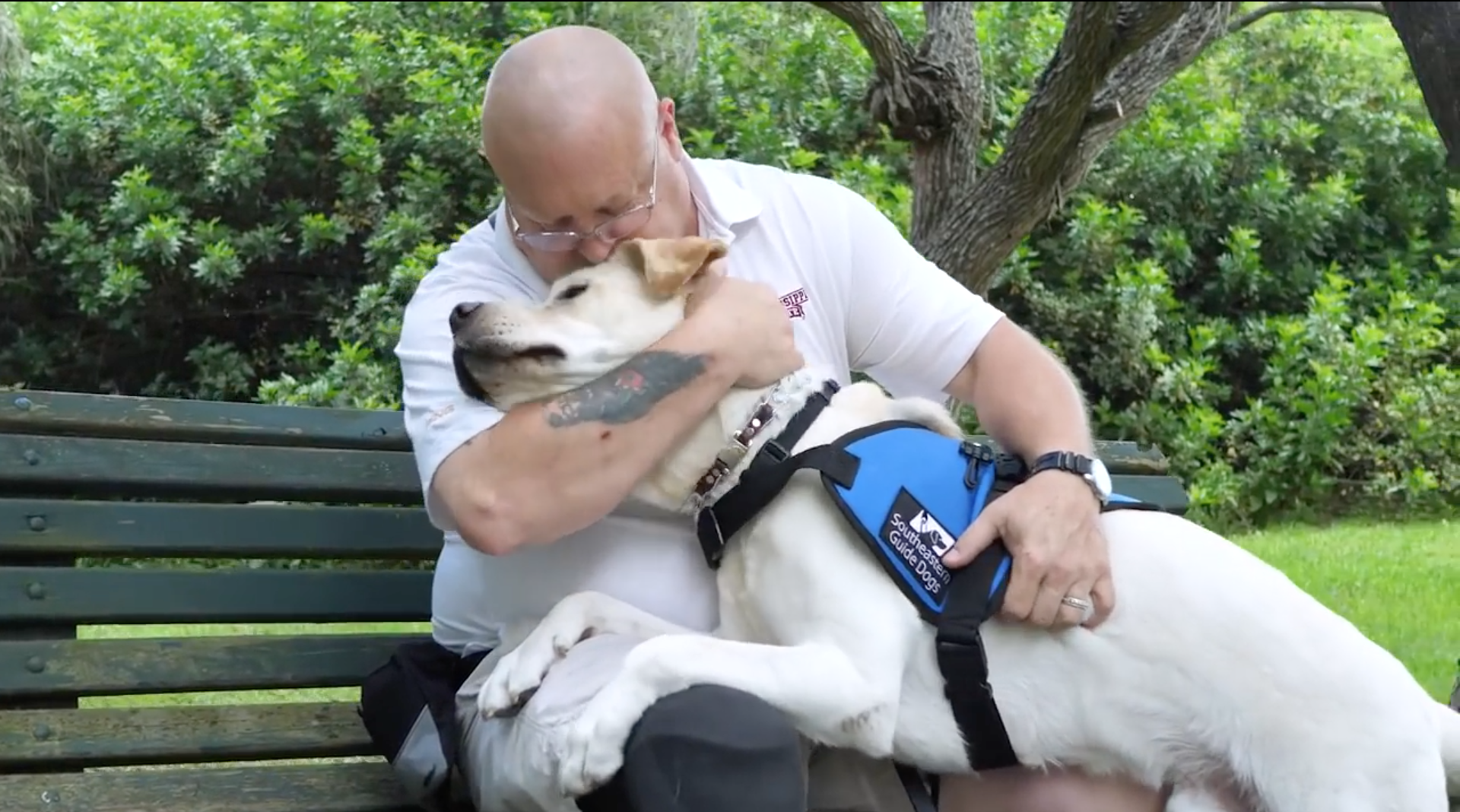 man sits on a bench with yellow lab service dogs two paws on his legs and kisses the top of his head