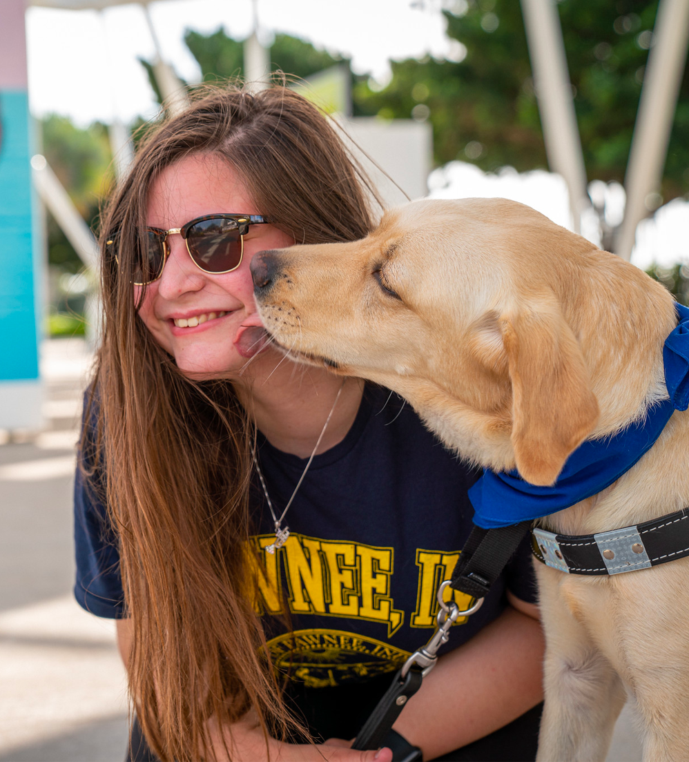 Teen girl smiles while being kissed by yellow lab guide dog