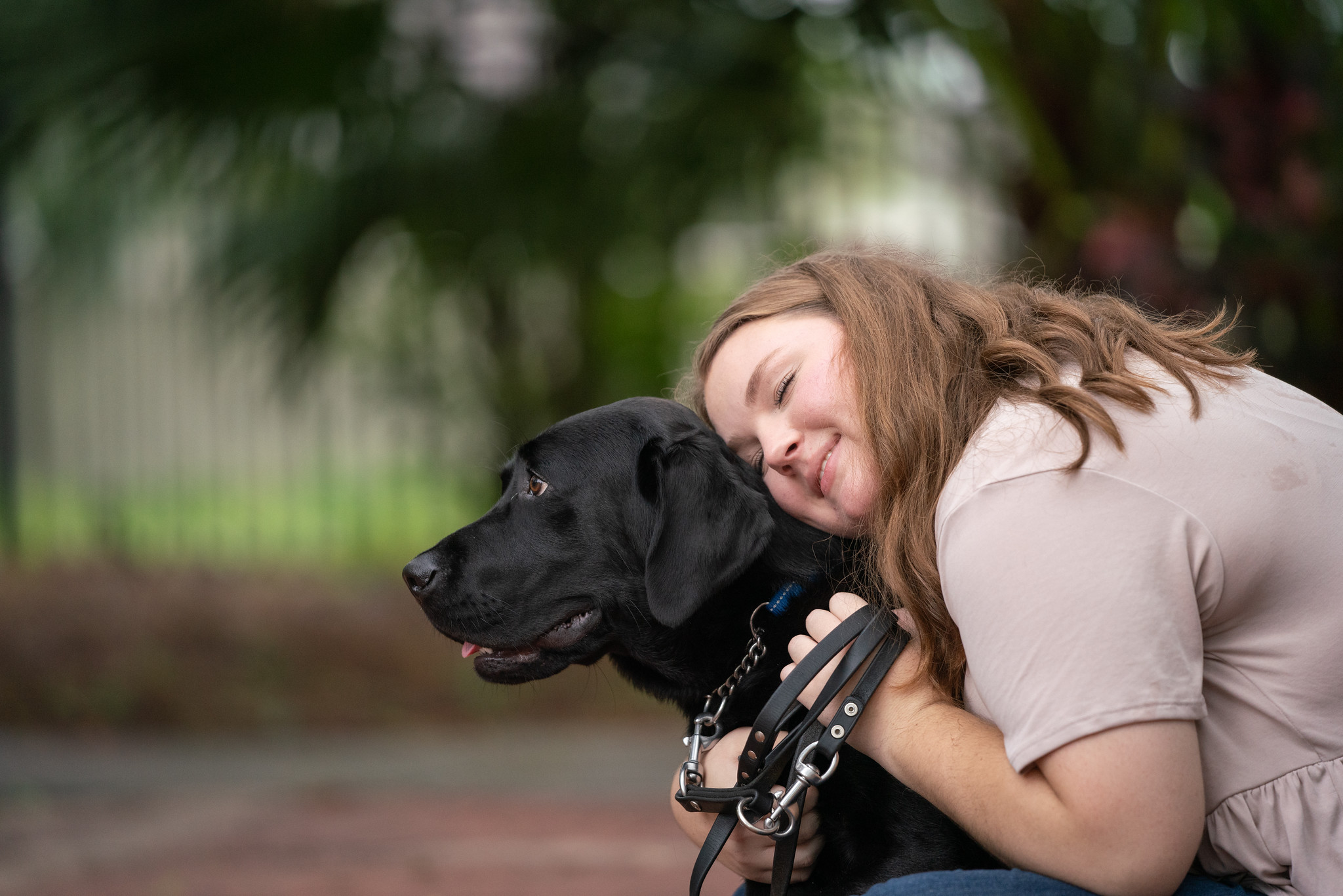 Girl smiles while she hugs black lab