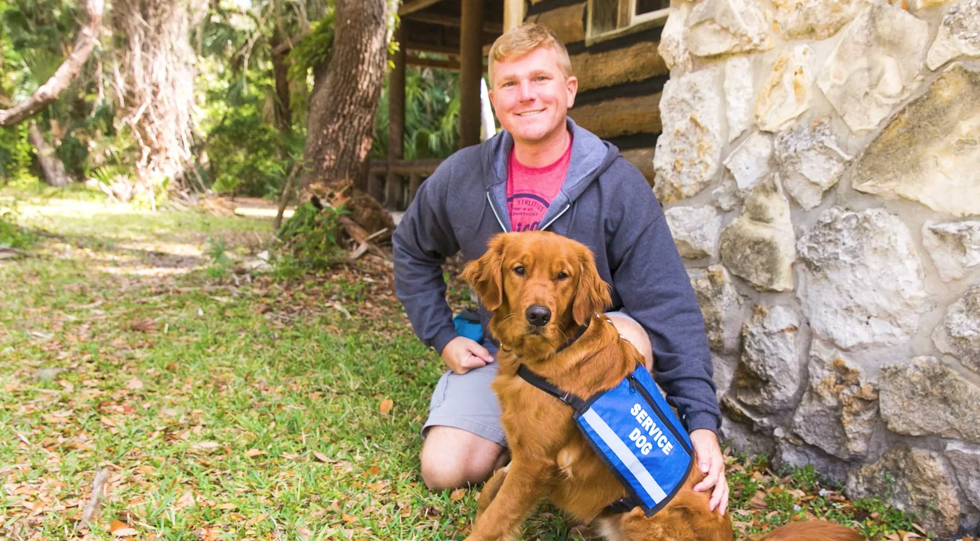 Man kneels and smiles while posed with golden retriever service dog