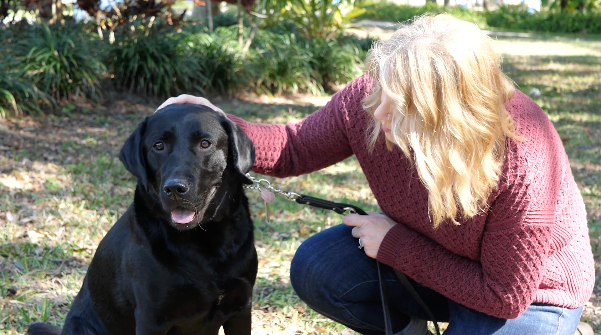 Woman kneels next to black lab and pets its head