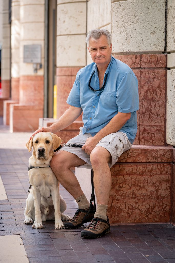 Arnold sits on red brick his hand resting on his yellow labs head. 
