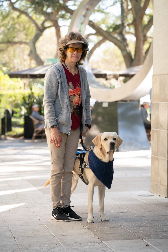 Chris stands with her guide dog in front of a large archway