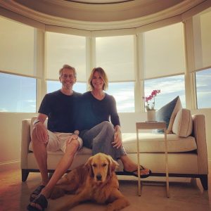 A couple sit on a couch with a Golden Retriever laying in front on them.