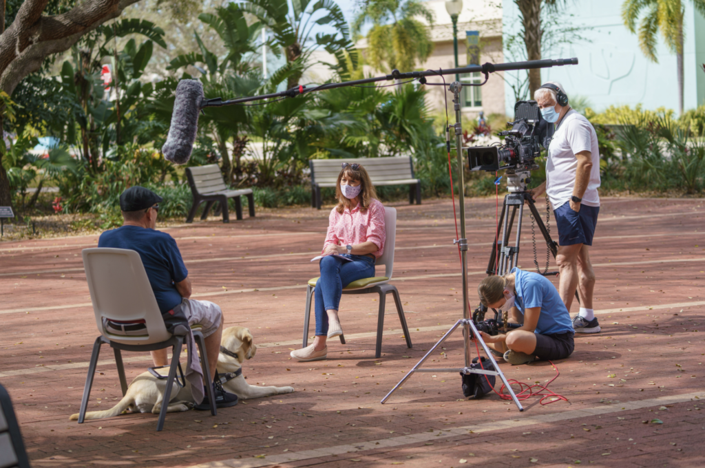 Jen sits interviewing a student as two camera men film and a boom mic leans overhead