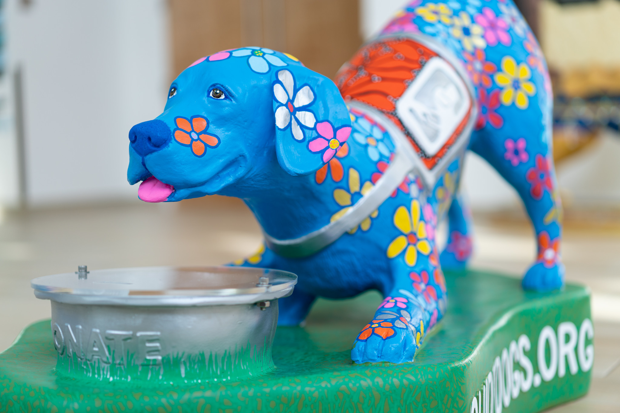 sculpture of dog in playful pose painted blue with flowers and a donate bowl