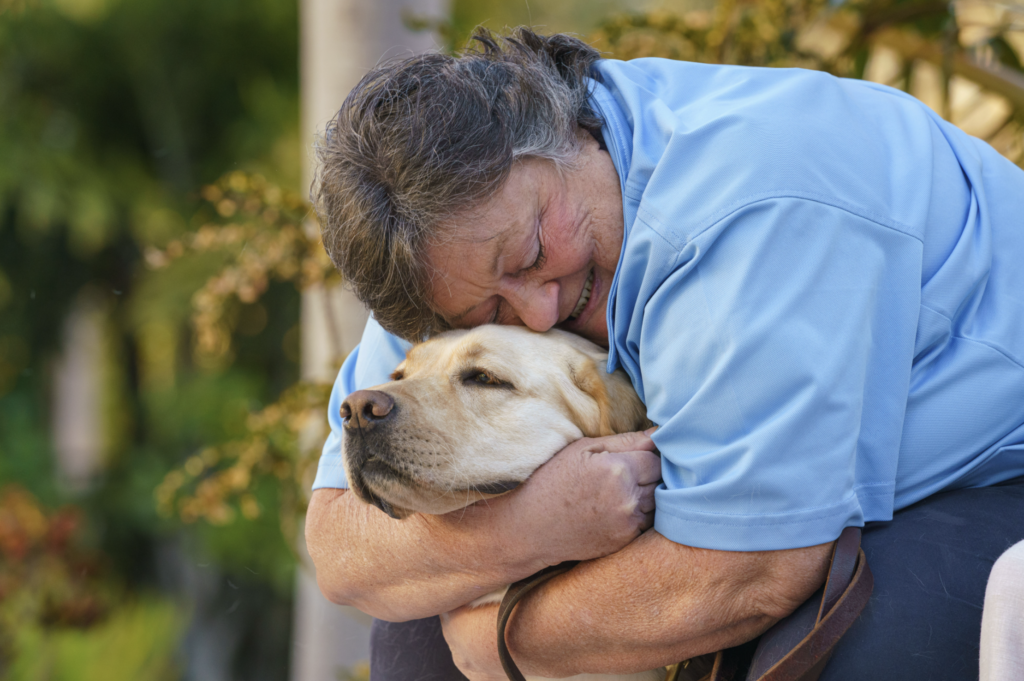 A puppy raiser embraces her dog with a large smile spread across her face