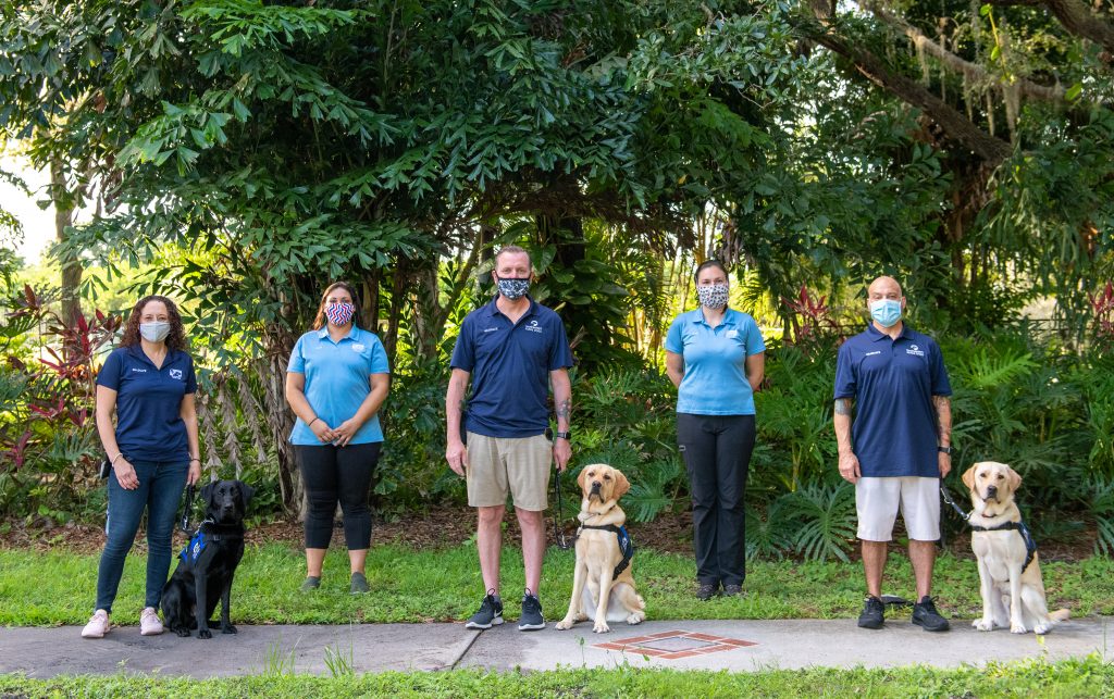 three graduates stand with their new dogs, the trainers stand with them.