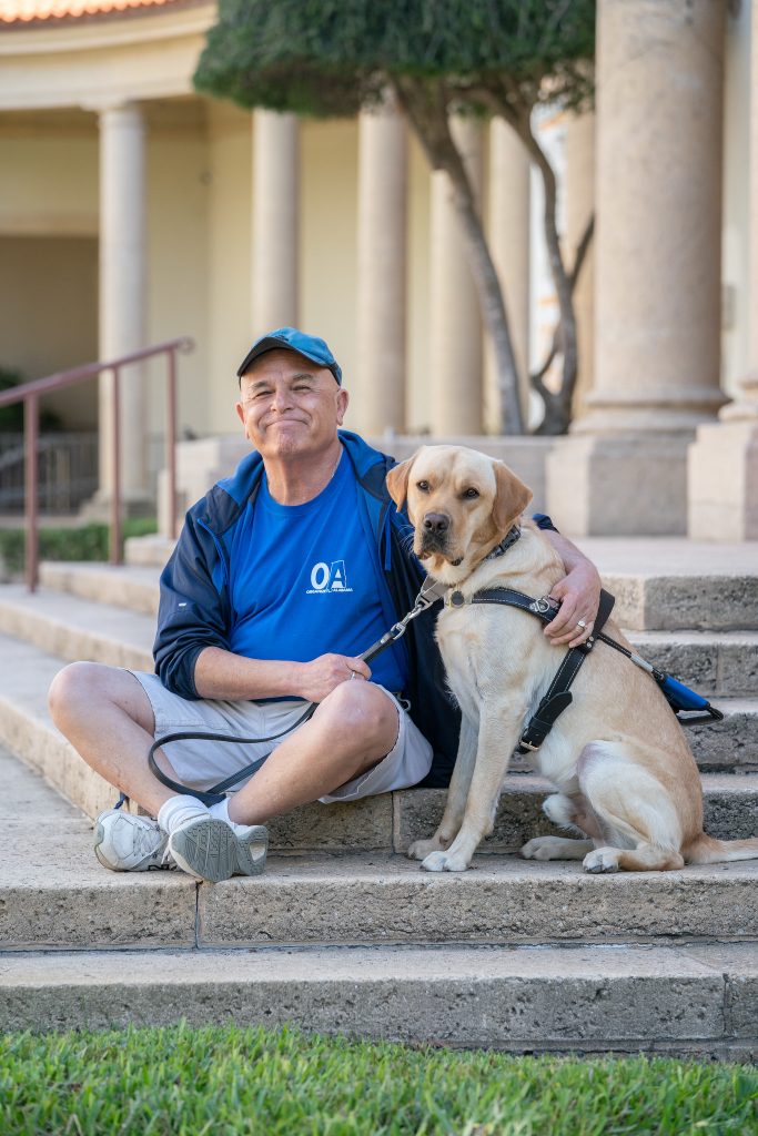 Simon sits on a set of stairs smiling as he hugs his dog