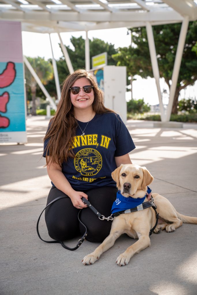 A young girl sits next to her yellow lab guide dog