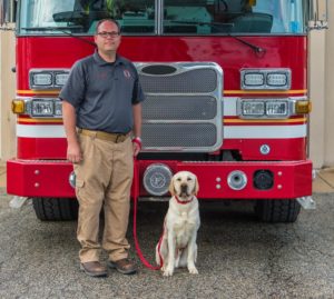 A firefighter and a yellow Lab standing in front of a red firetruck