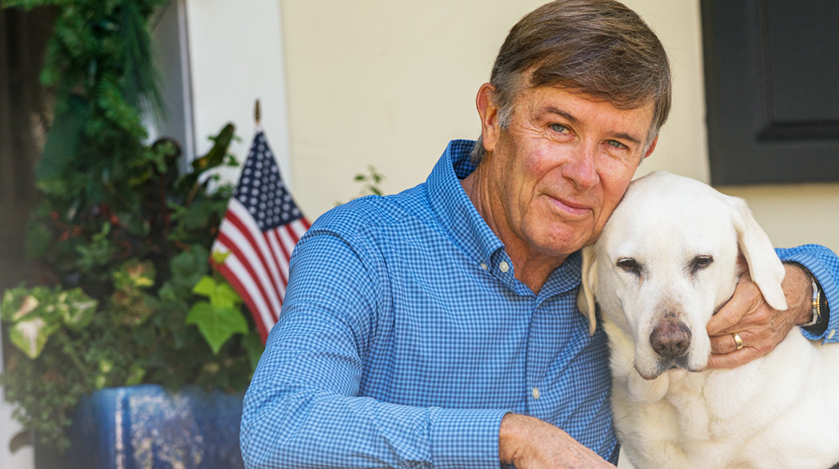 Joe Maguire and Ambassador Dog Darley sit and hug on the steps of his front porch.