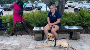 A photo of Emily Miller sitting on a bench with her guide dog Hugo