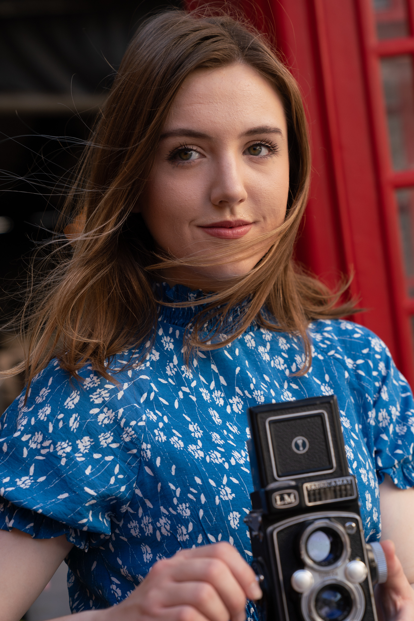 A young woman in a blue dress poses with a vintage camera