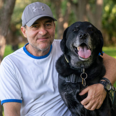 David Caras hugging his black Labrador retriever, service dog Bobb.
