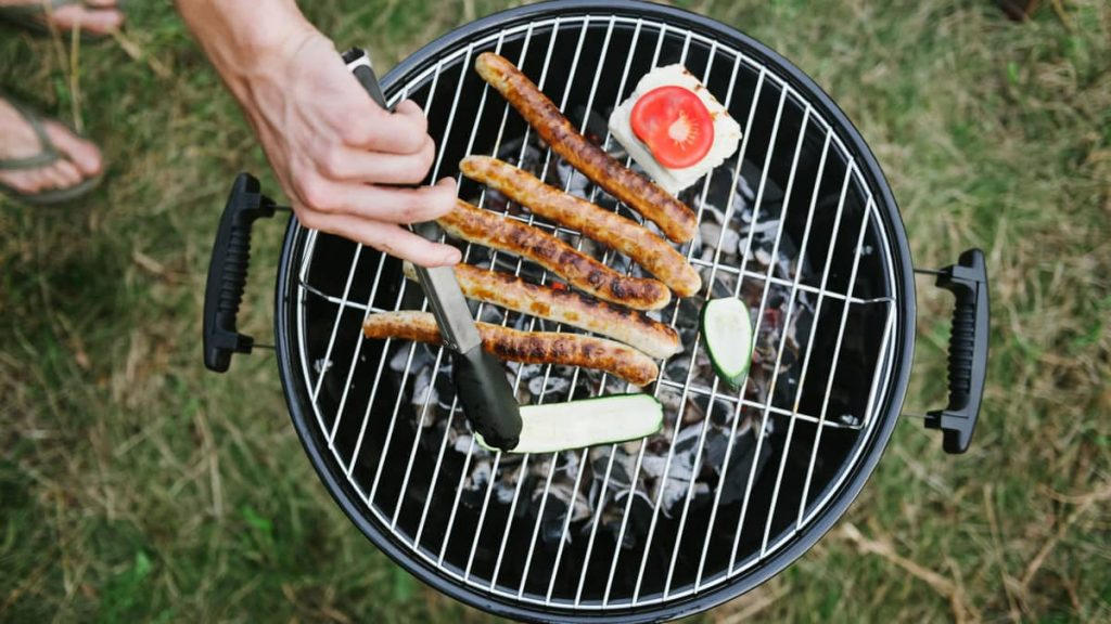 A close-up image of a man grilling hot dogs on his charcoal grill.