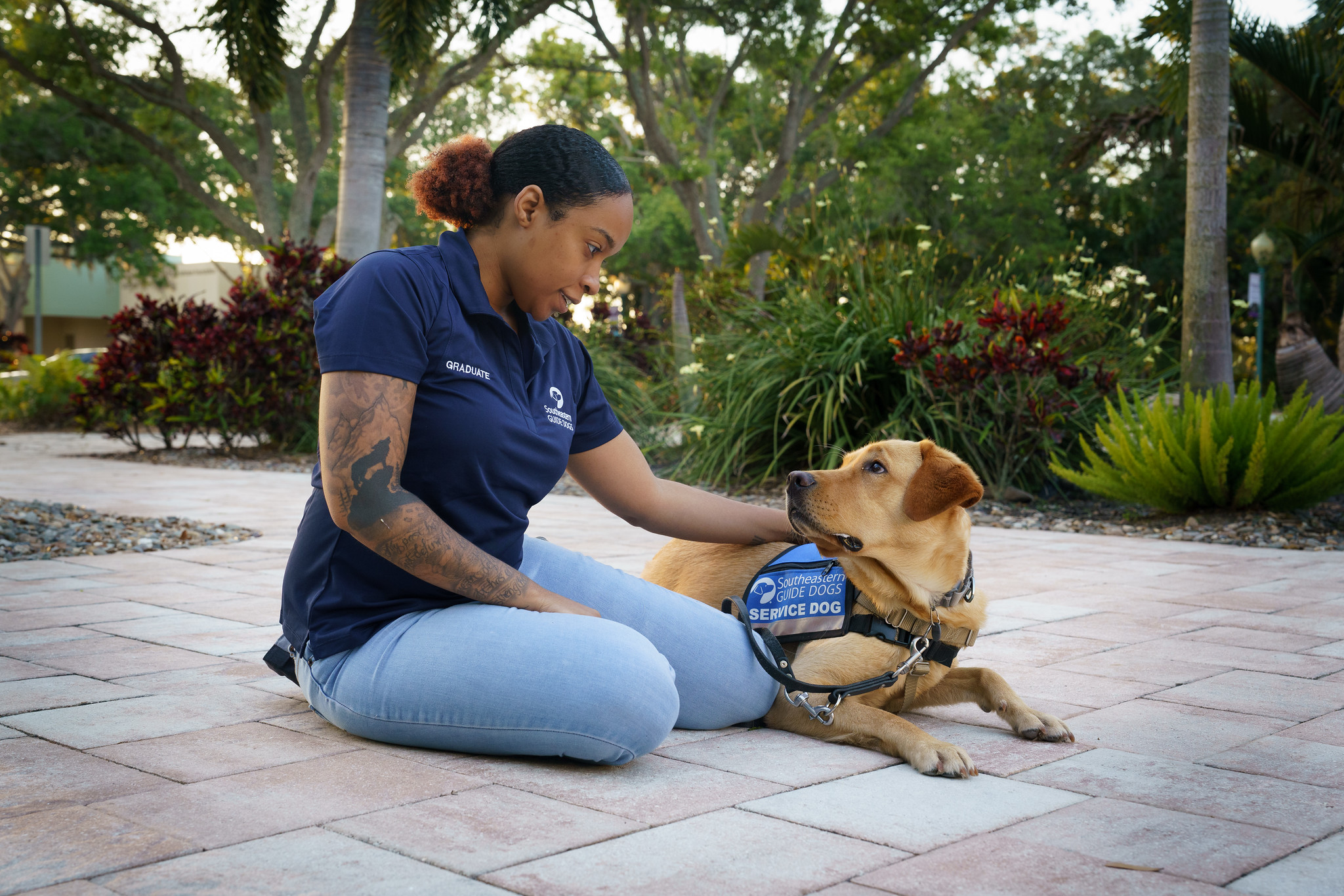 A female service dog owner sitting and petting her yellow lab lying next to her