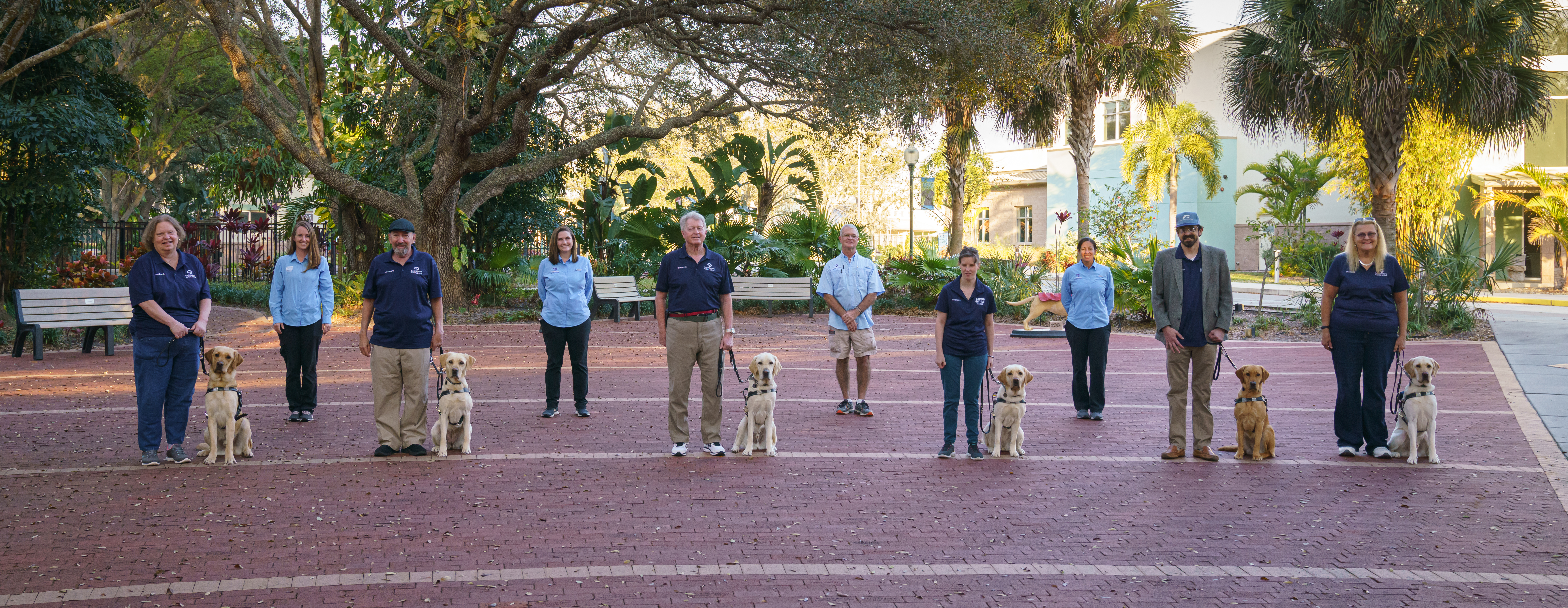 Six graduates stand with their assigned dogs with four dog trainers stacked behind them.